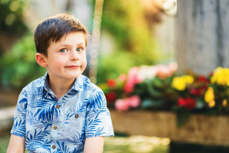 Outdoor summer portrait of adorable kid boy resting outdoors next to fountain on a very hot sunny day, wearing blue print shirtの写真素材