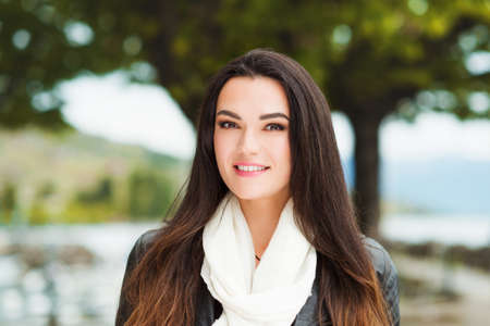 Outdoor portrait of beautiful brunette woman with long hair, wearing big white cashmere scarf and black leather jacketの写真素材