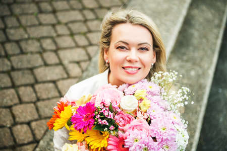 Outdoor close up portrait of blond woman holding big bouquet of nice fresh flowersの写真素材