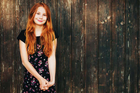 Outdoor fashion portrait of happy red-haired girl, posing against old wooden background
