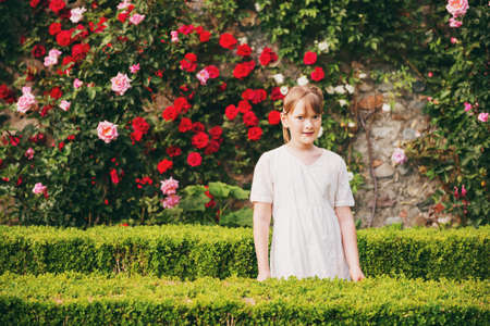 Adorable little girl playing in classical English tapiary garden, wearing white vintage style dressの写真素材