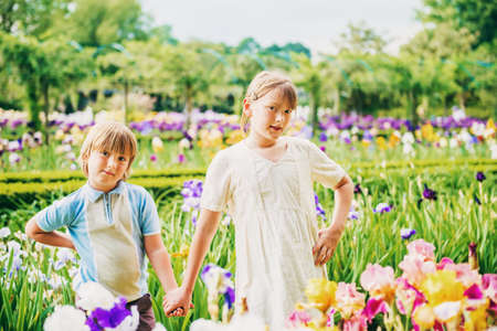 Group of two kids, little boy and girl, posing in beautiful garden, wearing retro style clothing,...