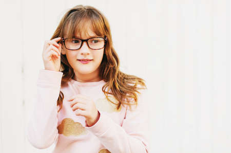 Outdoor portrait of a cute little 9 year old girl, wearing soft pink sweatshirt and glassesの写真素材