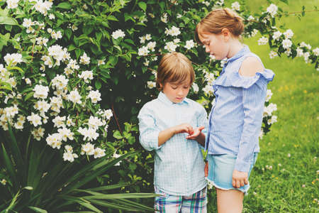 Two adorable kids playing together in spring garden, wearing fashion shirtsの写真素材