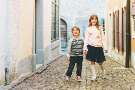 Outdoor portrait of adorable fashion kids, wearing sweatshirts, holding hands, walking together in a cityの写真素材