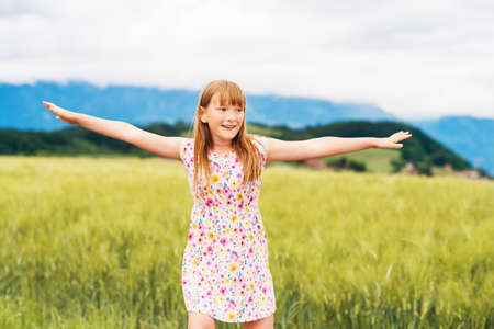 Little girl playing in green wheat field in summertime, wearing a dress, arms wide openの写真素材