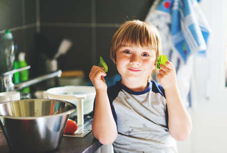 Adorable kid boy holding spinach leaves, child helping in the kitchenの写真素材