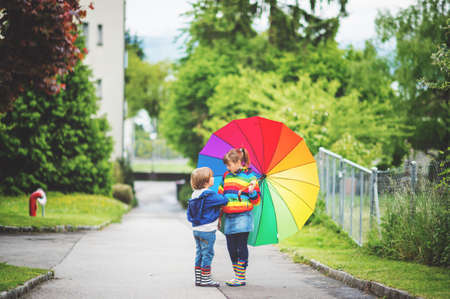 Two adorable kids playing outdoors with big colorful umbrellaの写真素材