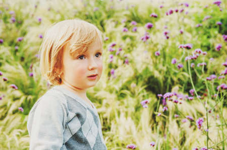 Adorable blond toddler boy playing in a garden, wearing grey pulloverの写真素材