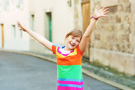 Happy smiling joyful kid girl with arms up playing on the streetの写真素材