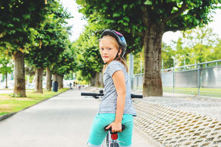 Kid girl sitting on the bicycle in the park, looking back over the shoulderの写真素材