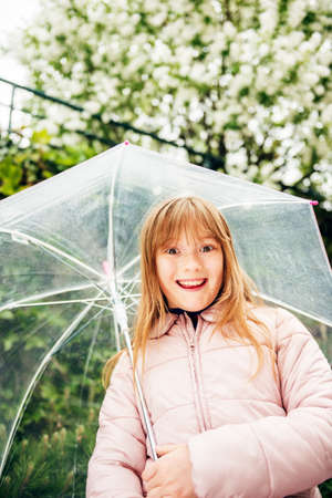 Happy kid girl playing under the rain, holding transparent umbrellaの写真素材