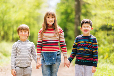 Group of three happy kid hiking in spring forest, two boys and one girl playing together outside, wearing pulloversの写真素材
