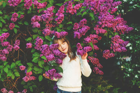 Adorable kid girl playing with blooming lilac flowers in spring garden, eyes closedの写真素材