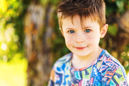 Outdoor close up portrait of adorable 5-6 year old red-haired boy with freckles on his faceの写真素材