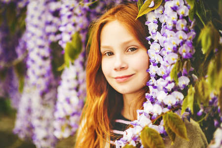 Close up portrait of adorable 9-10 year old red-haired kid girl posing in wisteriaの写真素材