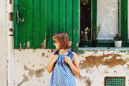 Funny little girl tourist on the streets of Provence, Wearing blue gingham dress, sunglasses and backpack. Travel with children concept. Image taken in Arles, Franceの写真素材