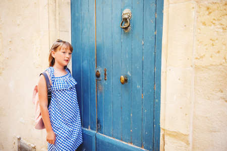 Pretty little girl tourist on the streets of Provence, Wearing blue gingham dress, sunglasses and backpack. Travel with children concept. Image taken in Arles, Franceの写真素材