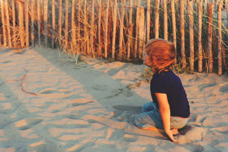 Funny kid boy resting on sand beach by the sea at sunset. Young child enjoying summer vacation on south of Franceの写真素材