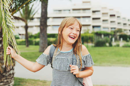 Happy laughing young kid girl enjoying summer vacation. Preteen 10 year old child wearing cold shoulder t-shirt and backpack. Travel with kidsの写真素材
