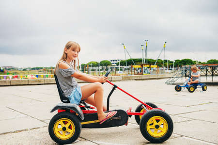 Two active little kids driving pedal race car. Outdoor summer activities for childrenの写真素材