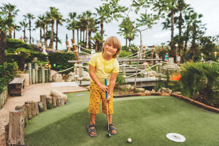 Funny kid boy playing mini golf, child enjoying summer vacationの写真素材