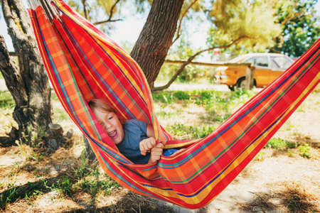 Funny little boy playing in hammock, child resting in gardenの写真素材