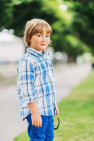 Outdoor fashion portrait of cute little 6 year old boy wearing blue plaid casual shirt and trousersの写真素材