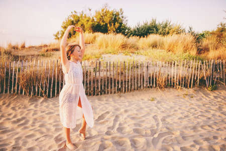 Beautiful kid girl dancing on sand beach by the sea at sunset. Preteen child enjoying summer vacation on south of Franceの写真素材