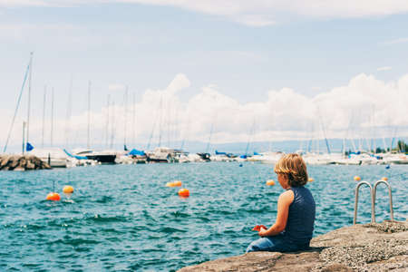 Funny little boy resting by lake Geneva in a small Lutry port, Switzerland. Back viewの写真素材
