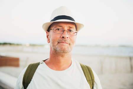 Handsome man on summer vacation by the sea, wearing hat, glasses and backpackの写真素材