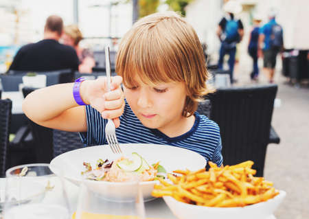 Little boy having lunch in the restaurant, child eating fresh salmon salad and french friesの写真素材