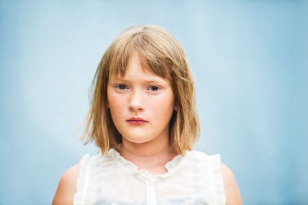 Close up portrait of adorable little girl with short bob haircut standing against blue backgroundの写真素材