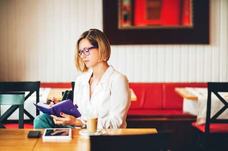 Young successful business woman writing in agenda, girl working in coffee shopの写真素材
