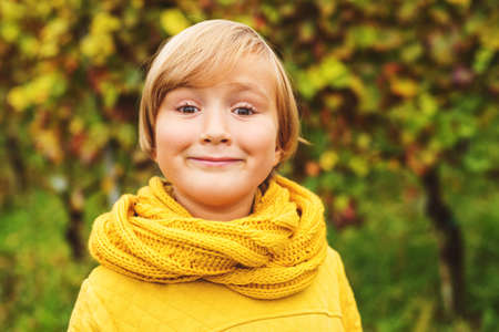 Autumn close up portrait of adorable little boy wearing yellow warm sweatshirt and knitted scarf