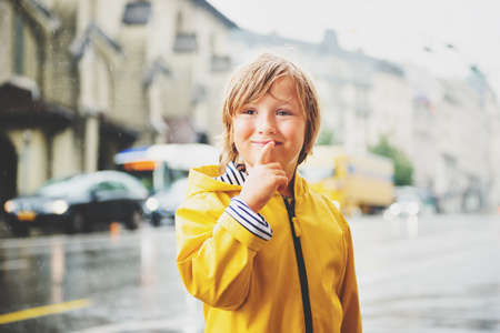 Cute little boy playing under the rain in a city, wearing bright yellow raincoat with hood. Image taken in Saint-Francois square, Lausanne, Switzerlandの写真素材