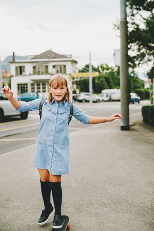 Funny little schoolgirl riding skateboard outside, back to school concept, film look toned imageの写真素材
