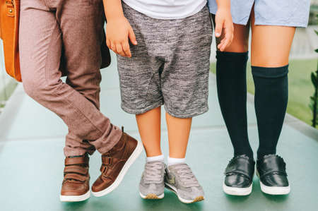 Fashion shoes on kids. Three pairs of children's feet wearing comfortable and fashion trainers. Back...