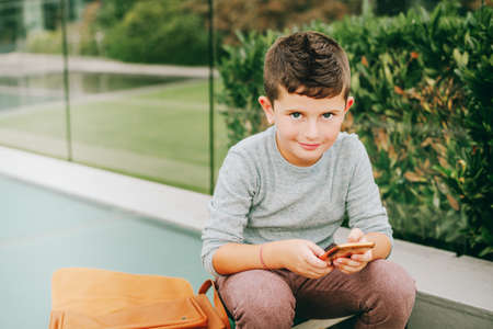Outdoor portrait of cute little schoolboy playing with smartphoneの写真素材