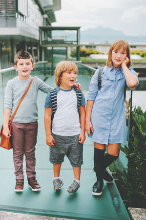 Group of 3 funny schoolkids posing outdoors, wearing backpacks. Back to school concept. Fashion for childrenの写真素材