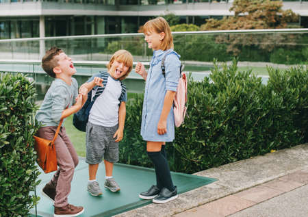 Group of 3 kids playing Rock, Paper, Scissors game on schoolyard. Back to school concept, fashion...
