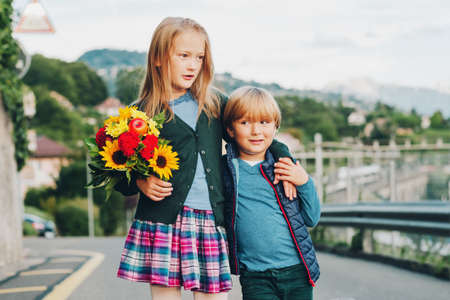 Outdoor portrait of a cute little kids with beautiful bouquet of autumn flowers. School fashion for children, schoolwearの写真素材