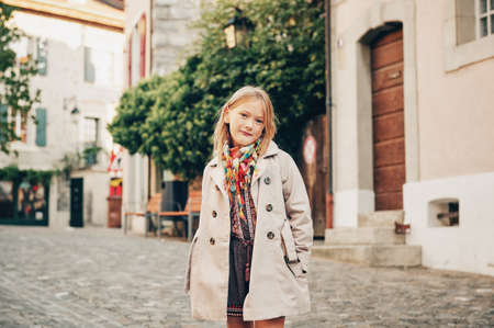 Outdoor fashion portrait of 8-9 year old hipster girl wearing stylish trench coat