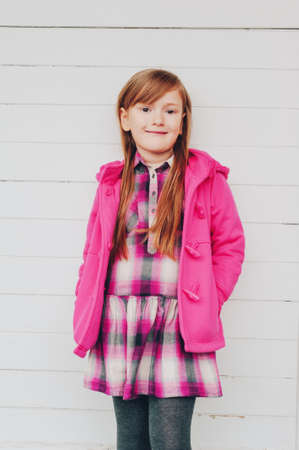 Outdoor portrait of pretty little girl wearing pink coat, autumn fashion for kids, posing against white backgroundの写真素材
