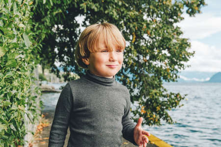 Outdoor portrait of funny little boy walking next to beautiful lake Geneva, wearing grey turtleneck shirtの写真素材