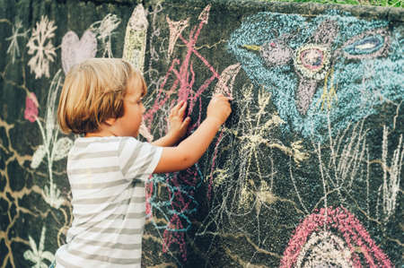 Adorable little boy drawing with a chalk outdoors. Outside activities for childrenの写真素材
