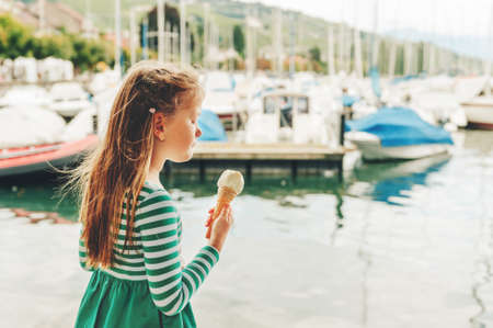 Outdoor portrait of funny little girl eating ice cream by the lakeの写真素材