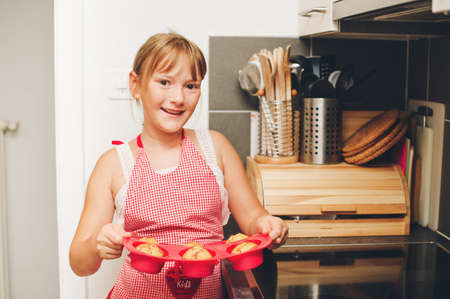 Happy little kid girl holding tray of freshly baked muffins, cooking with childrenの写真素材