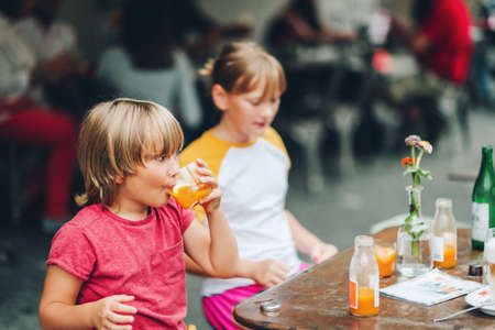 Group of two funny kids having drink in cafe, outdoorsの写真素材