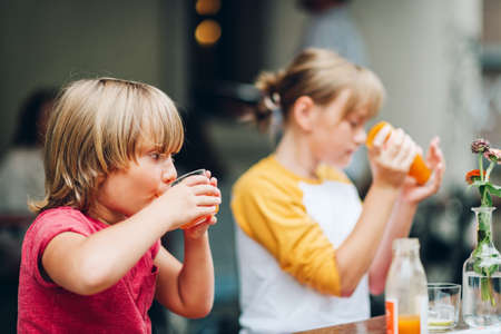 Group of two funny kids having drink in cafe, outdoorsの写真素材